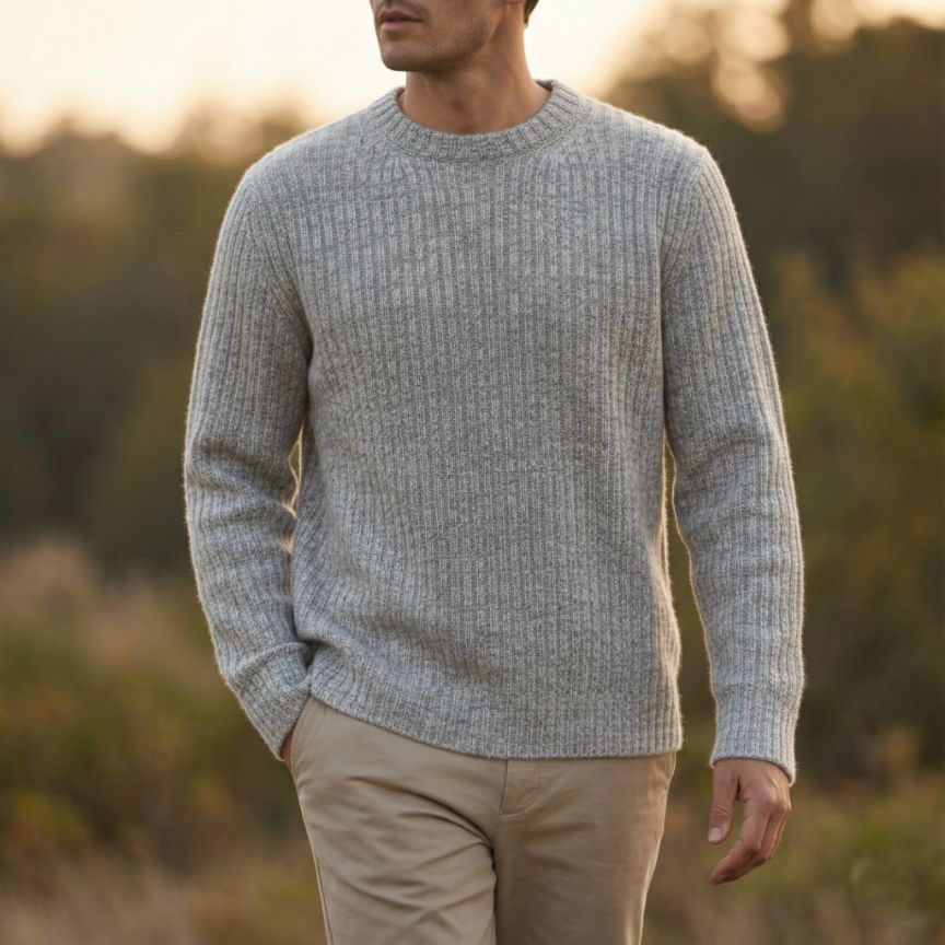 Man wearing a gray sweater and beige pants standing in a natural setting with blurred background