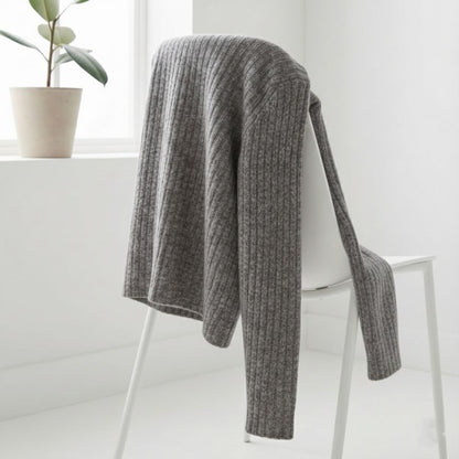 Gray knitted blanket draped over a chair in a minimalistic room with a plant in the background.