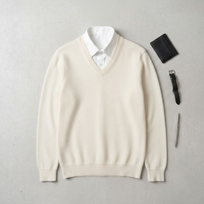 Beige sweater with white shirt, wallet, pen, and watch on a light gray background