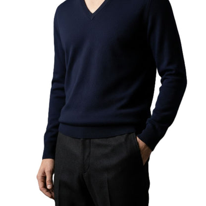 Person wearing a navy V-neck sweater and dark pants on a white background