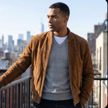Man wearing a brown jacket and gray shirt on a rooftop with city skyline in the background