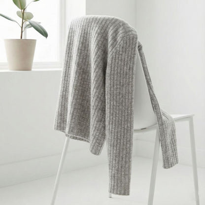 Gray knitted blanket draped over a white chair with a plant in the background