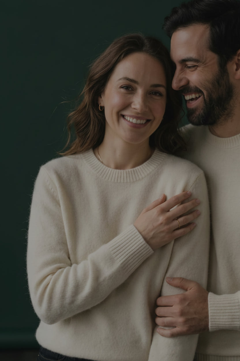 Couple in cream sweaters embracing against a green background